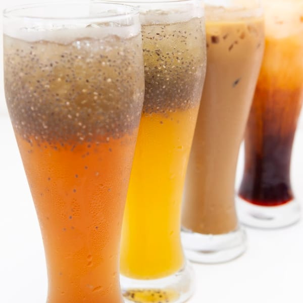 Four tall glasses of Vietnamese drinks, including orange, yellow, and brown beverages with chia seeds.