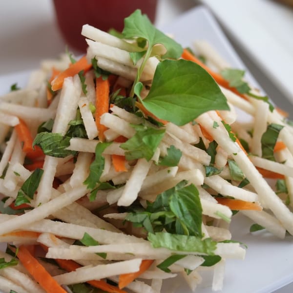 Close-up of a Vietnamese salad with shredded daikon, carrots, and fresh herbs on a white plate.