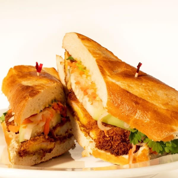 Two halves of a Vietnamese banh mi sandwich with crispy fried protein, fresh vegetables, and cilantro.