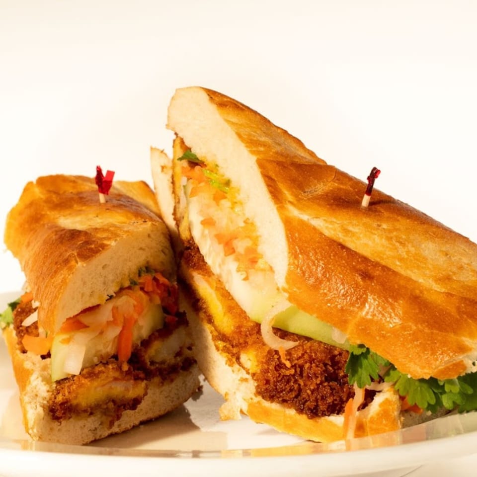 Two halves of a Vietnamese banh mi sandwich with crispy fried protein, fresh vegetables, and cilantro.