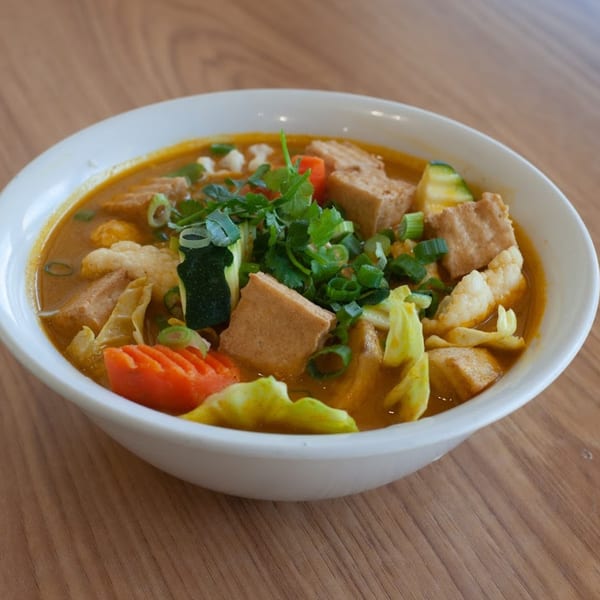 A vibrant bowl of Vietnamese curry with tofu, vegetables, and herbs in a white bowl.