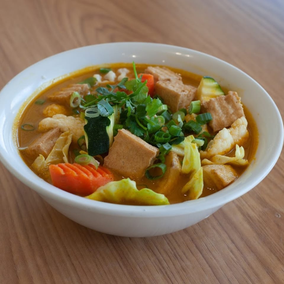 A vibrant bowl of Vietnamese curry with tofu, vegetables, and herbs in a white bowl.