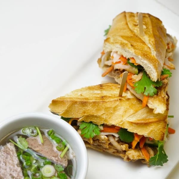 Two halves of a Vietnamese banh mi sandwich with a side of pho soup.